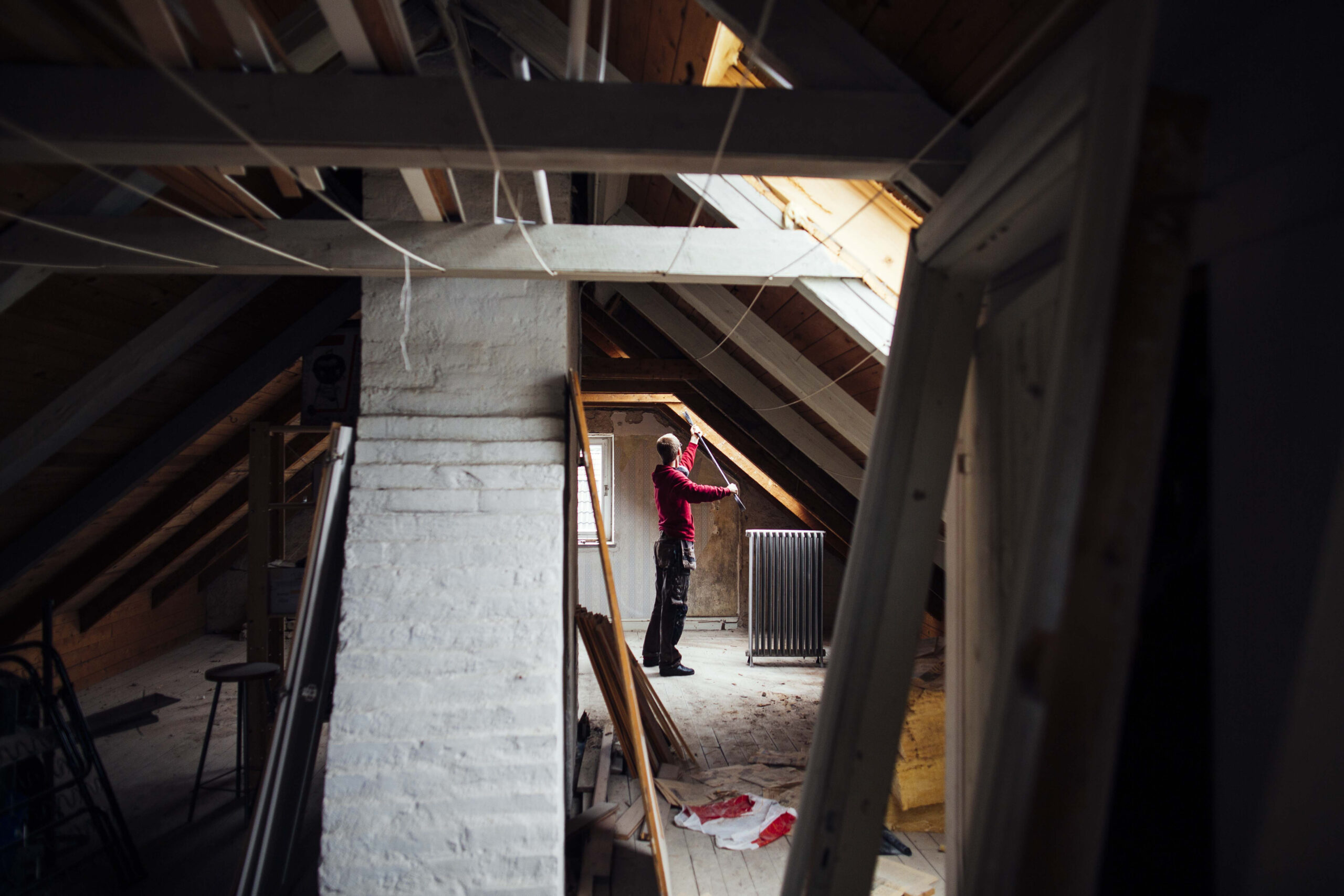Person renovating an attic space, inspecting the area with visible construction materials and tools, emphasizing attic restoration after pest damage.